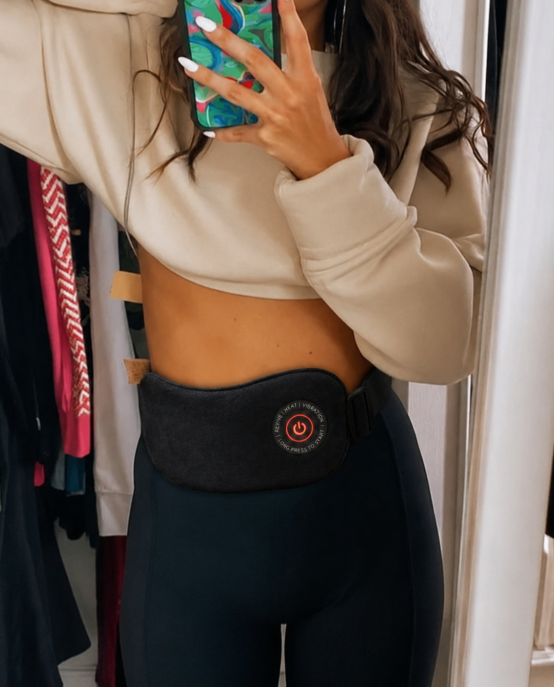 Woman taking a mirror selfie wearing the SŌLA heat wrap under a cropped top
